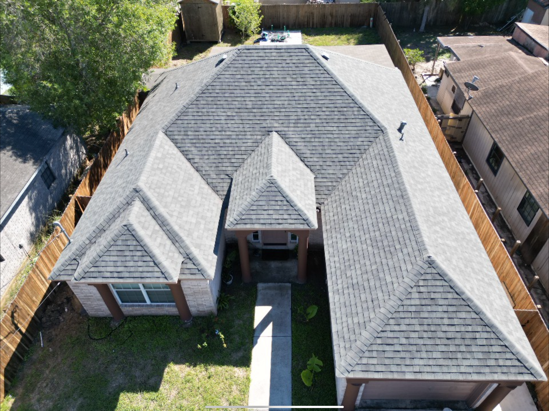 Aerial view of a gray-roofed suburban house with a central walkway and front lawn