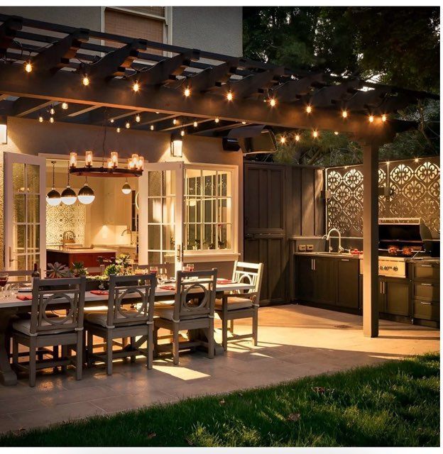Outdoor patio dining area with string lights, long table, and outdoor kitchen at dusk