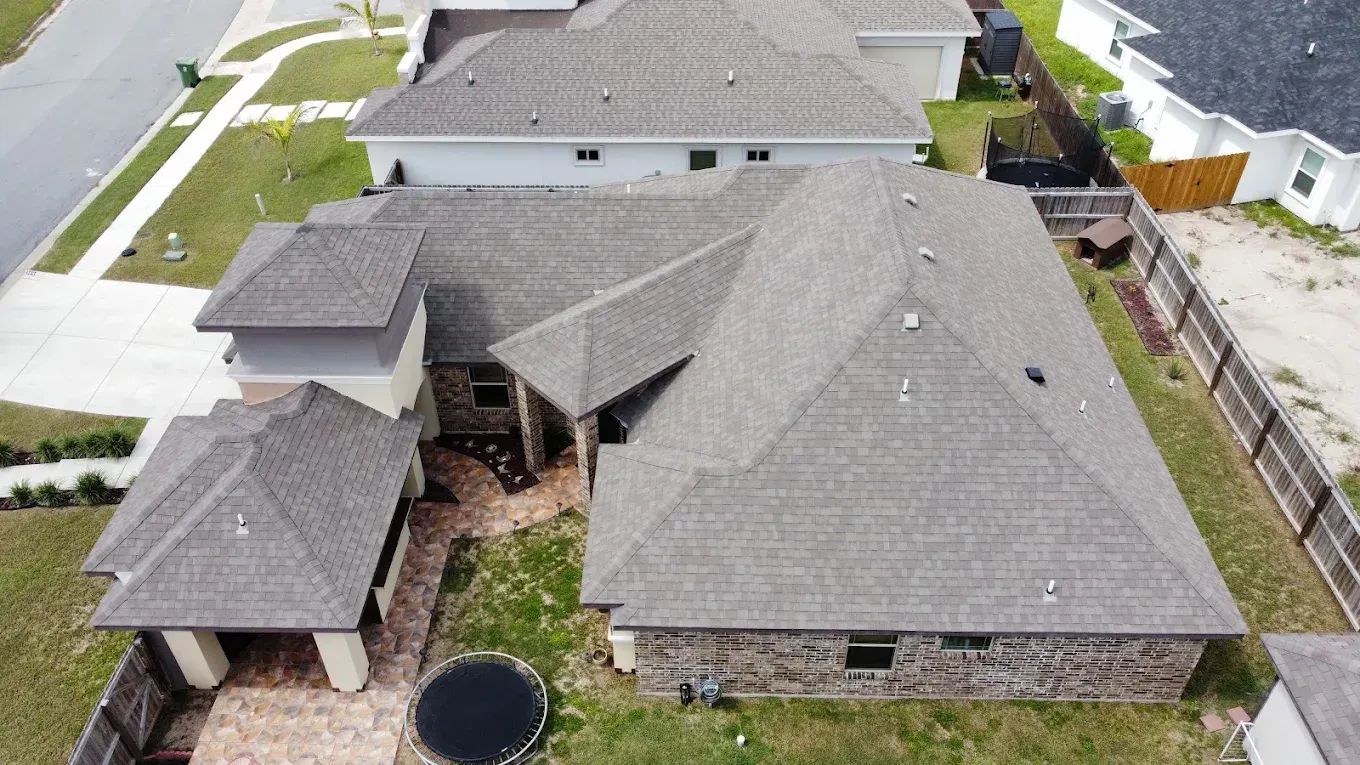 Aerial view of a gray-roofed suburban house with a small patio and fenced backyard.