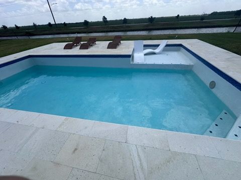 Modern backyard pool with turquoise water, white stone decking, and a lounge chair shelf overlooking open fields