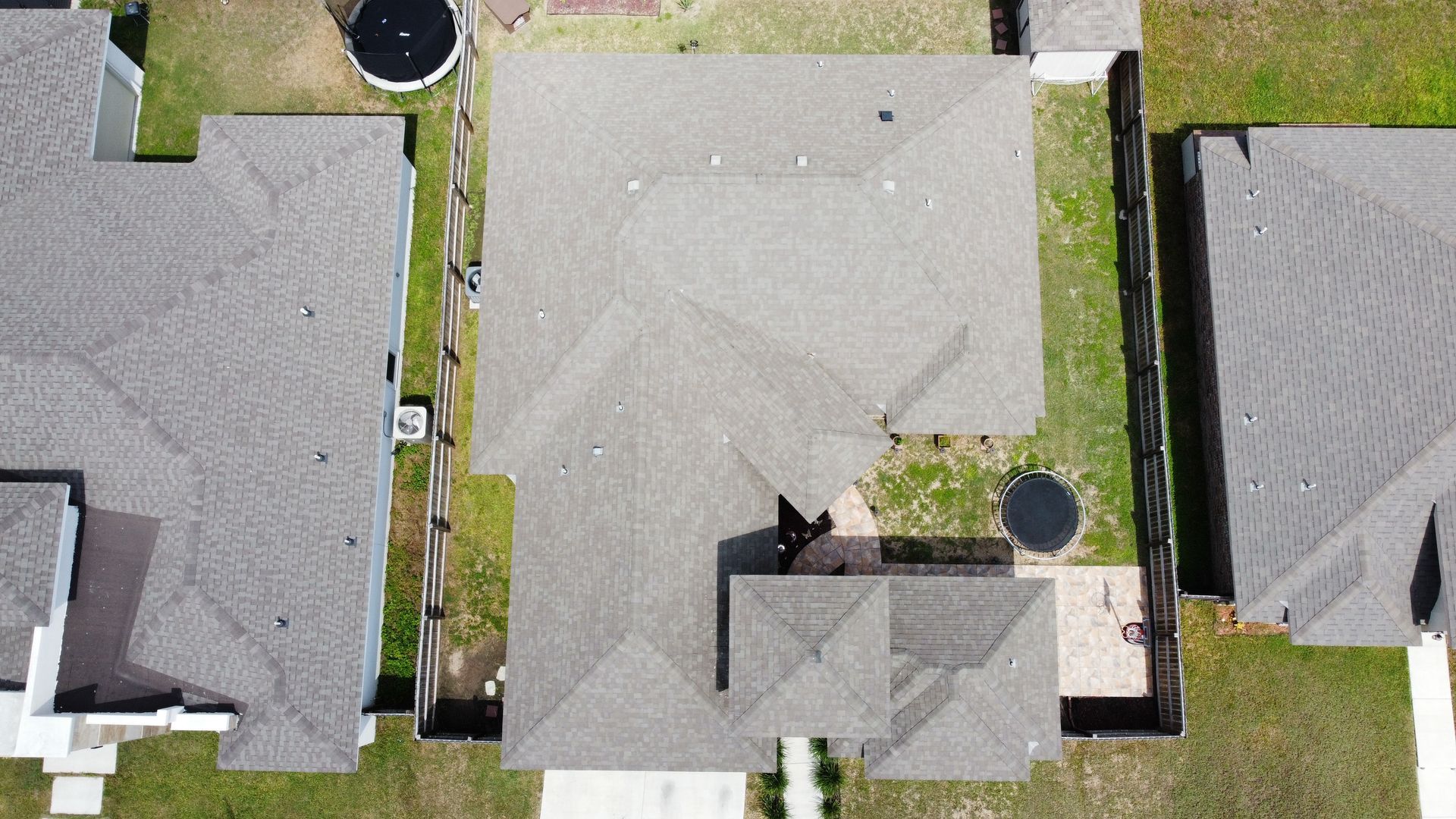 Aerial view of three suburban houses with gray roofs and lawns, separated by narrow driveways and trees.