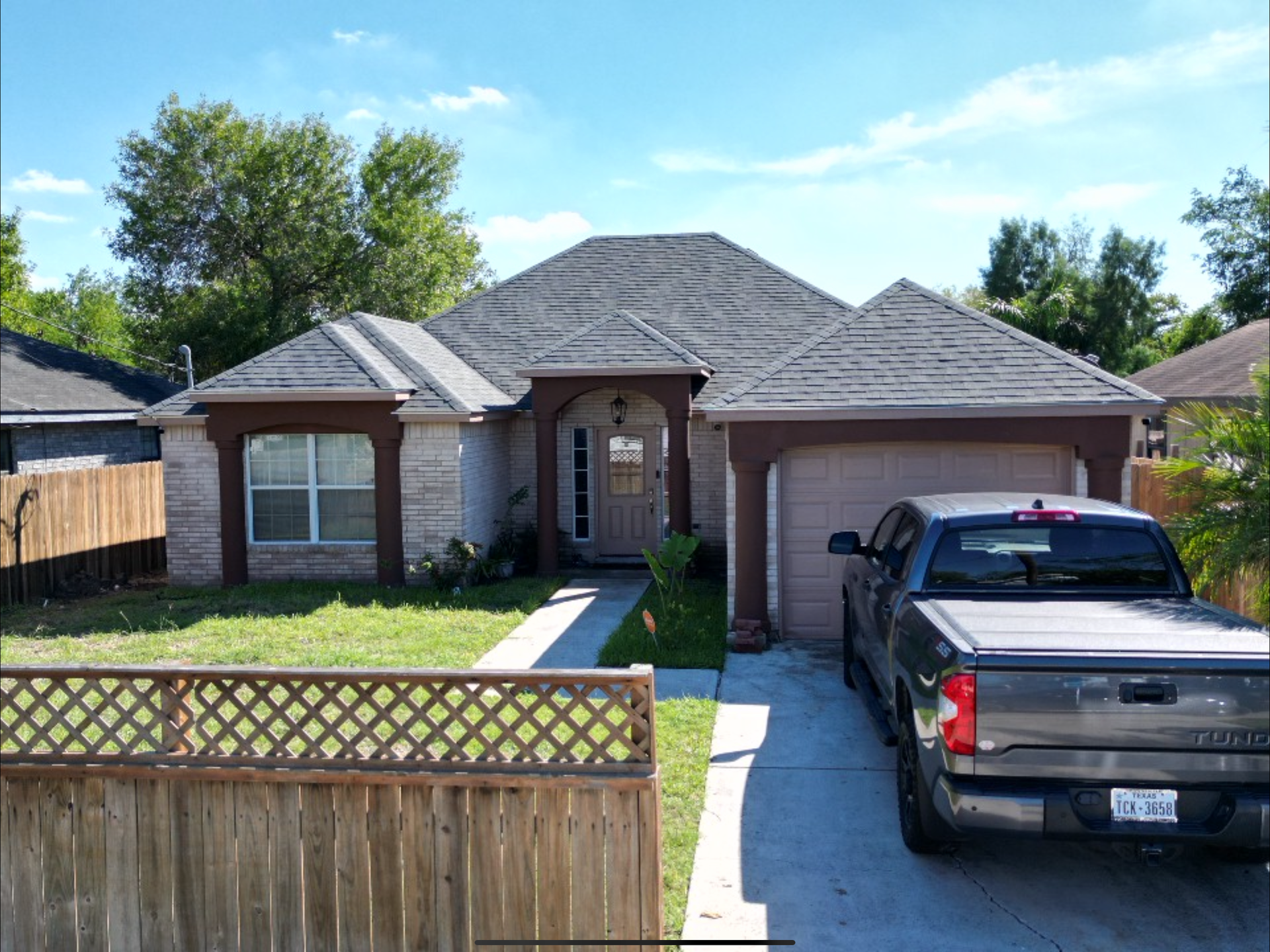 Single-story suburban house with a driveway, black pickup truck, and wooden fence in front.