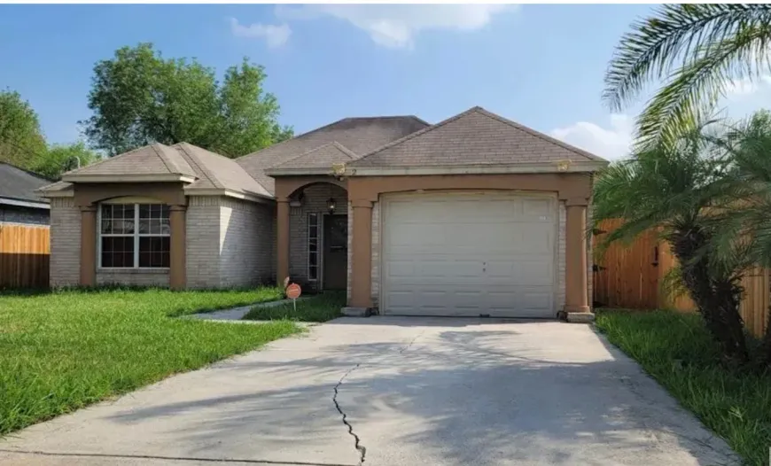 Suburban single-story house with a two-car garage, driveway, and green lawn under a sunny sky
