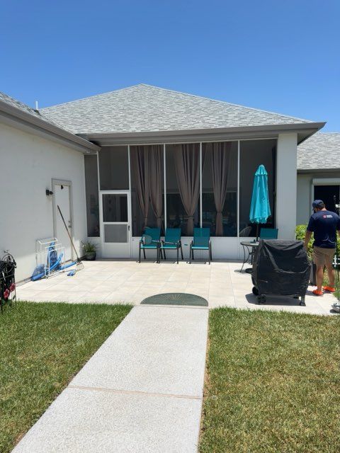 Backyard patio with chairs, sliding doors, and a person near a covered grill under a blue umbrella