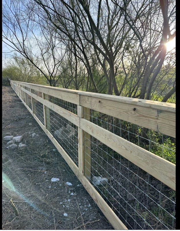 Wooden and wire fence along a dirt path beside leafless trees in sunlight