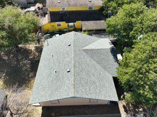 Aerial view of a gray-roofed house surrounded by trees and yellow buildings.