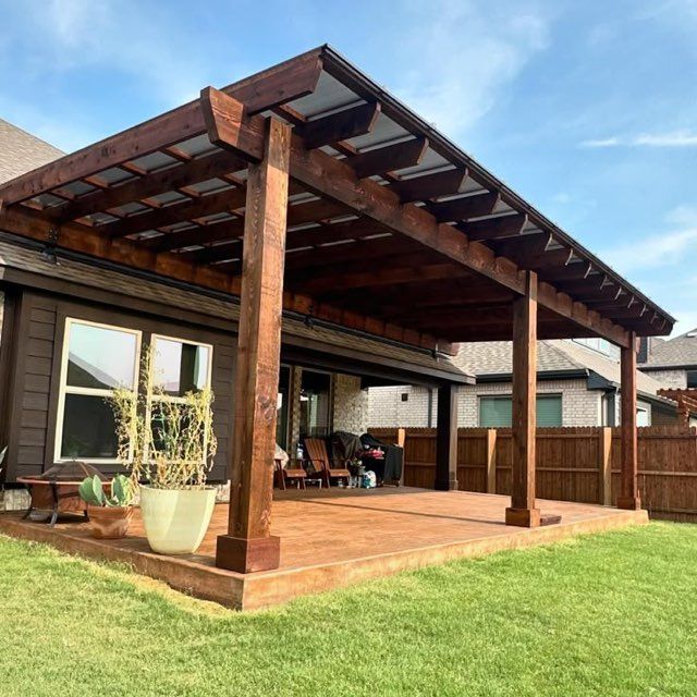 Modern wooden patio pergola with deck, potted plants, and a grassy backyard beneath a blue sky