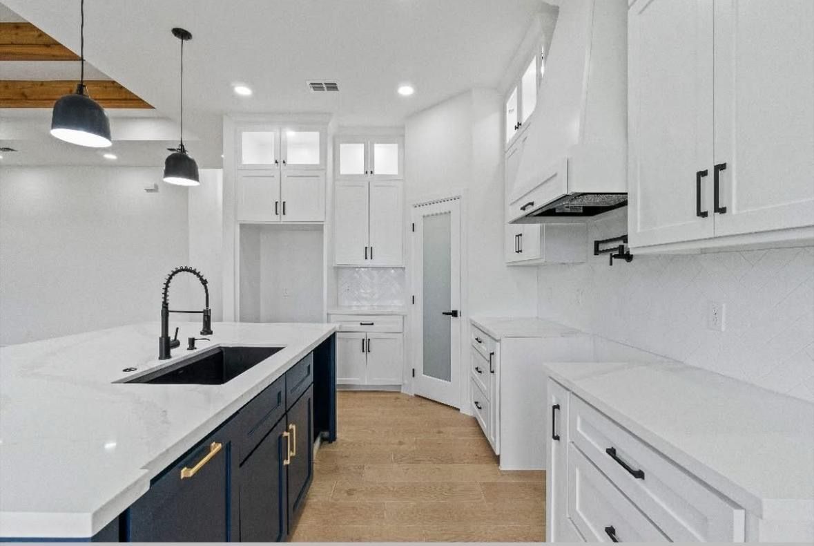 Bright modern kitchen with white cabinets, navy island, marble counters, and pendant lights