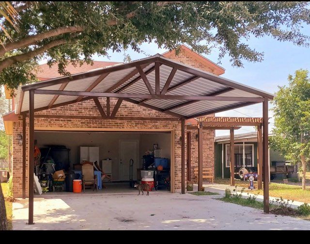 Brick garage with open front, exposed metal roof trusses, and household items inside, under a leafy tree