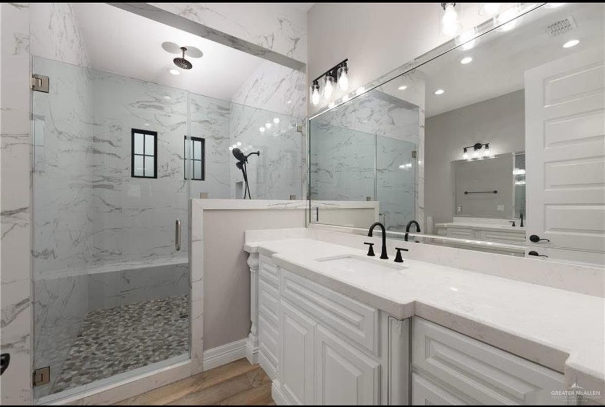 Bright modern bathroom with a glass shower, marble-look tile, and large vanity mirror