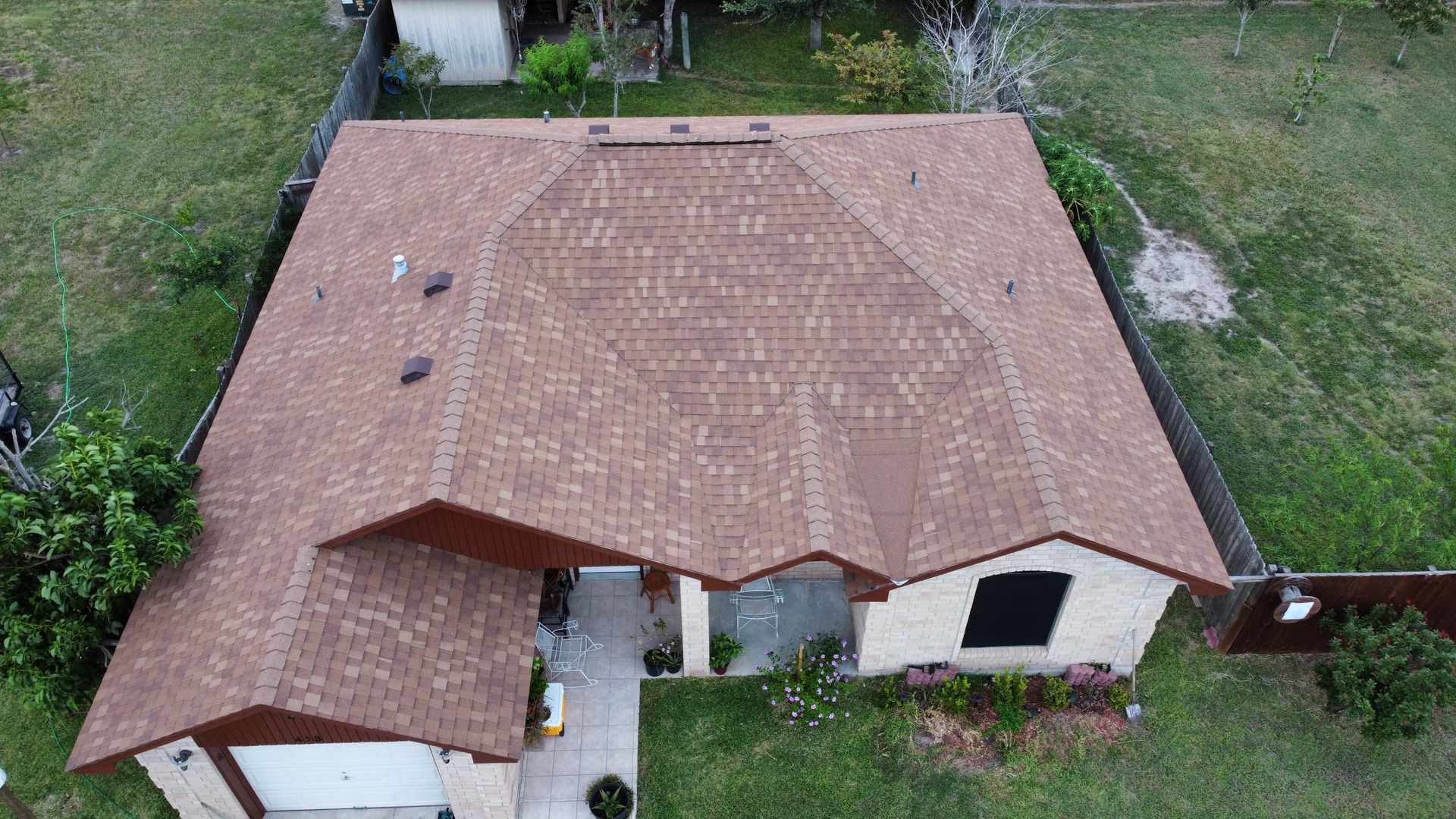 Aerial view of a house with a reddish-brown roof, driveway, and grassy yard.