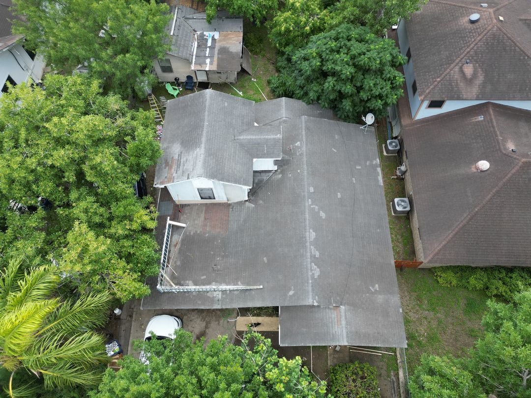 Aerial view of a gray-roofed house surrounded by dense green trees and neighboring homes.