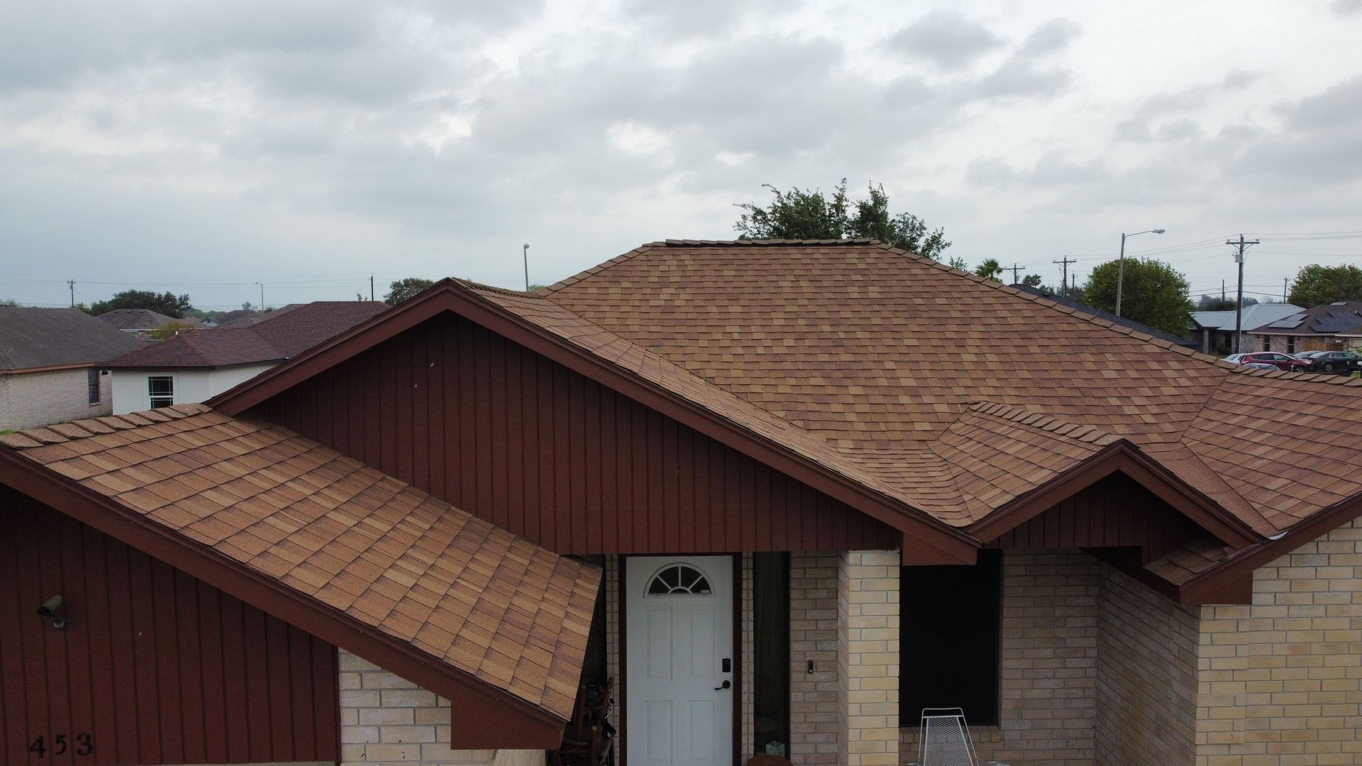 Suburban house with brown shingle roof and beige walls under a cloudy sky