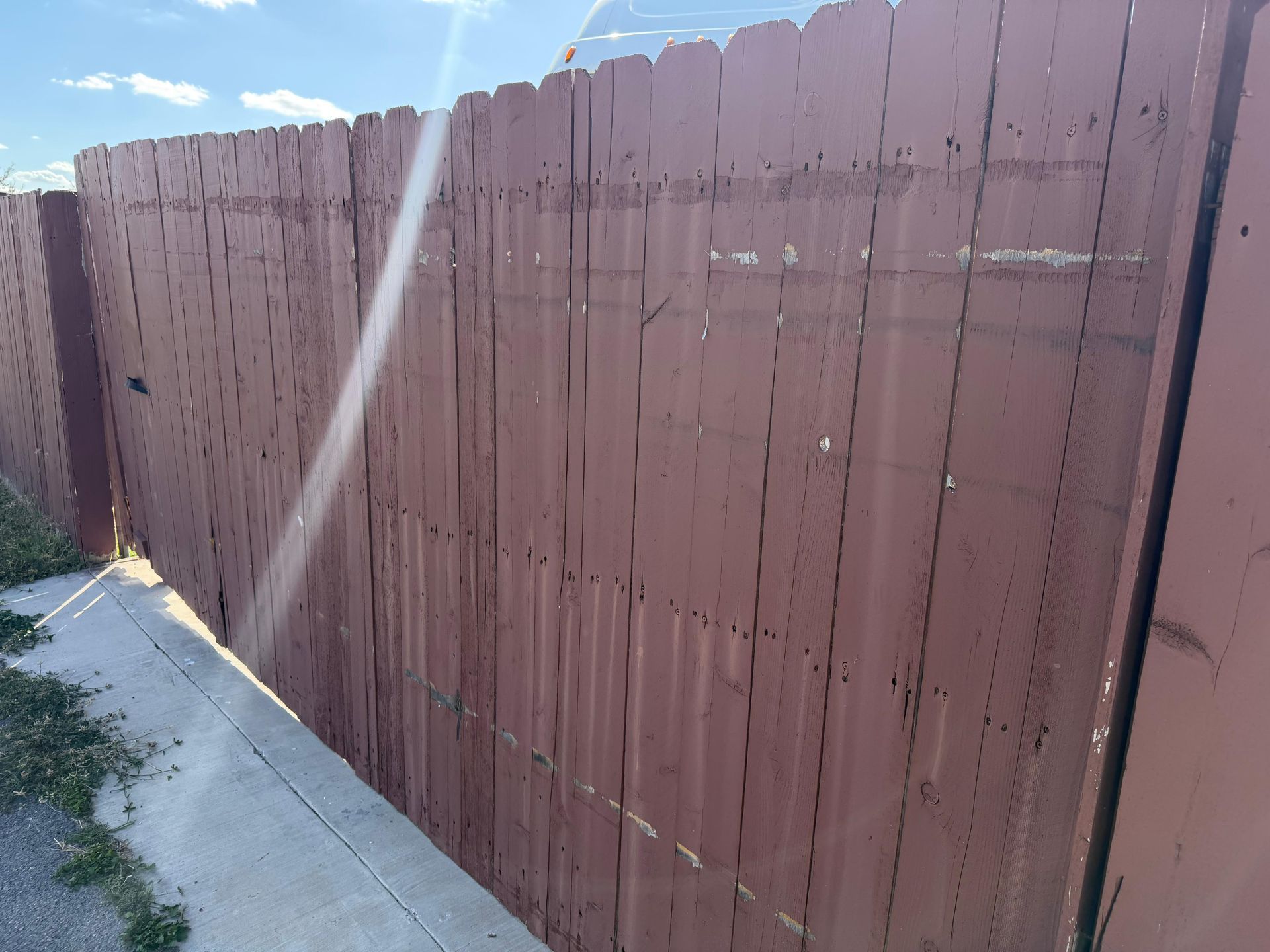 Sunlit wooden privacy fence along a concrete sidewalk on a clear day