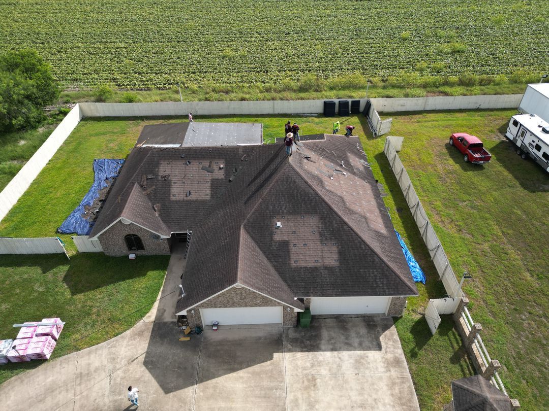 Aerial view of a house with a dark roof, driveway, lawn, and a red vehicle beside it.