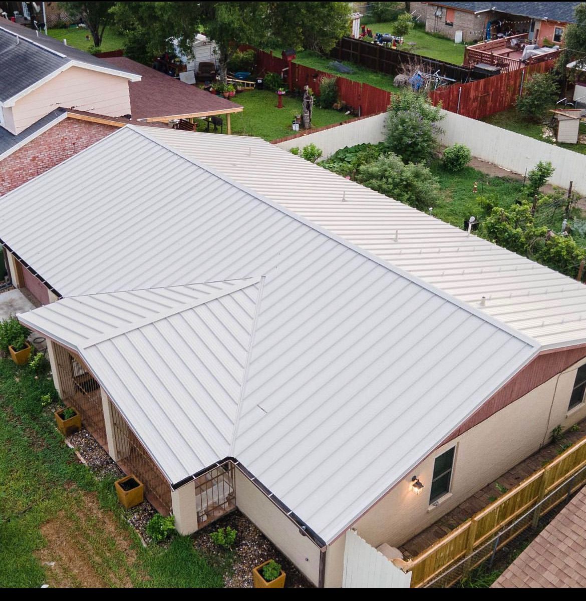 Aerial view of a house with a light metal roof and surrounding green yard.