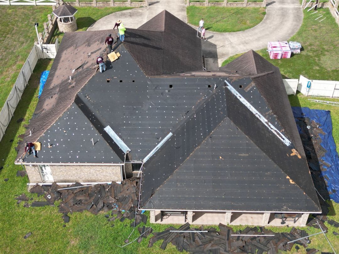 Aerial view of a house with a dark roof, with workers inspecting it during repairs