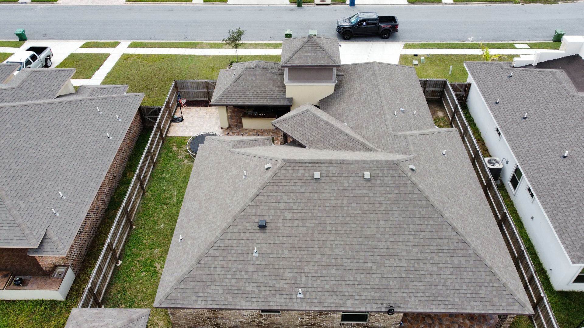Aerial view of several gray-roofed suburban houses with a street and parked car.