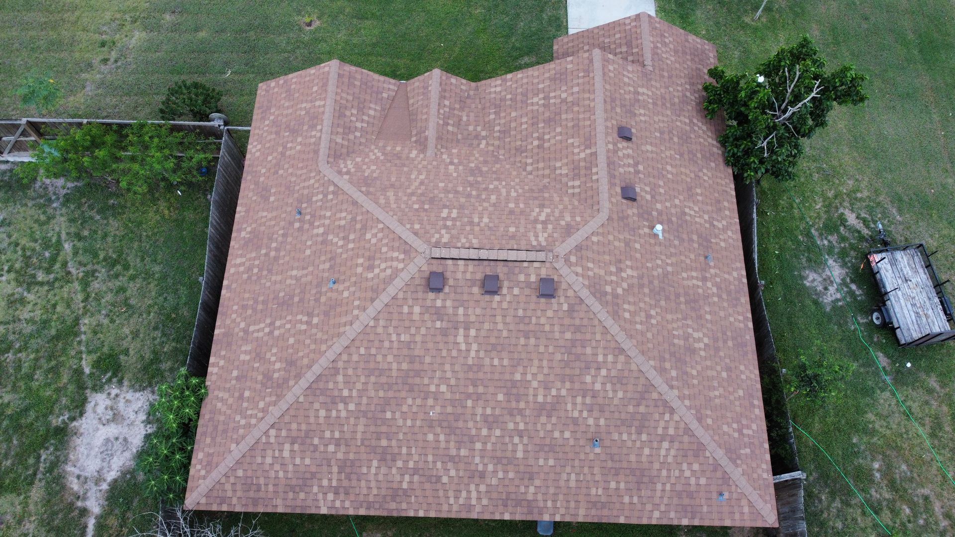 Aerial view of a tan shingled house roof with vents, surrounded by grass and a driveway.