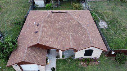 Aerial view of a single-story house with a brown shingled roof and a small front walkway surrounded by grass.