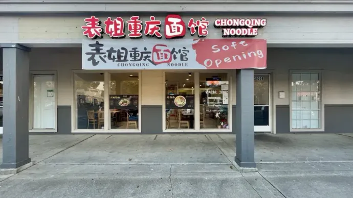 Storefront of Chongqing Noodle restaurant with red signage and a “Now Open!” banner under an awning
