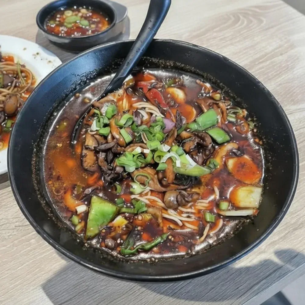 Bowl of dark sauce noodles topped with cucumber and scallions on a restaurant table