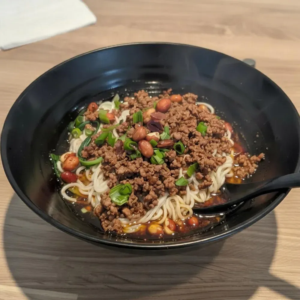 Black bowl of minced meat noodles with green onions and chili on a wooden table