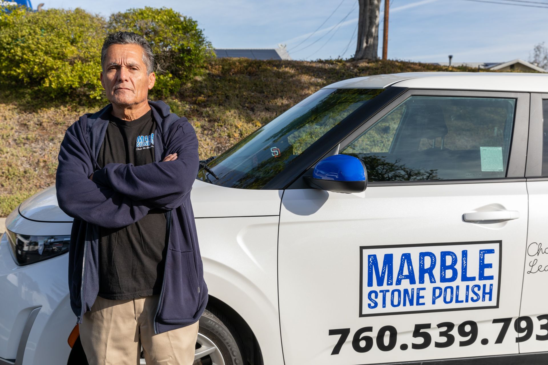 A person standing with arms crossed next to a white car featuring the text 