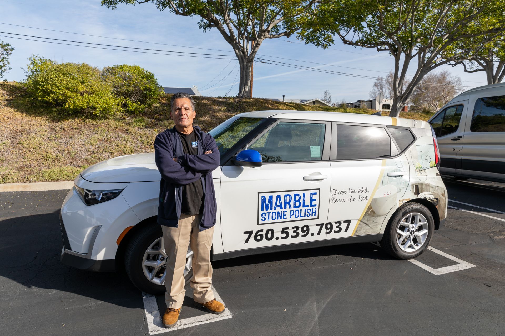 A man stands with arms crossed next to a white service car labeled 