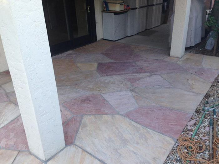 A patio floor made of multicolored, irregularly shaped flagstones arranged in a pattern between two white pillars.