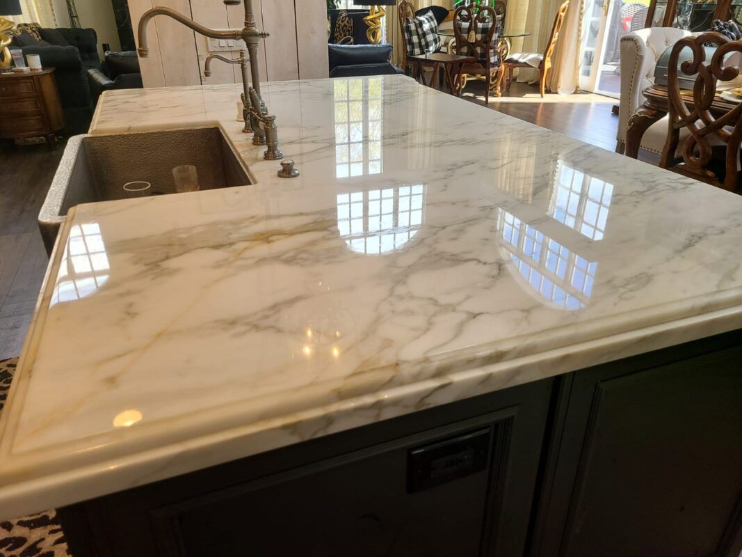 A close-up of a glossy, white marble kitchen island countertop with a built-in sink and a metal faucet.