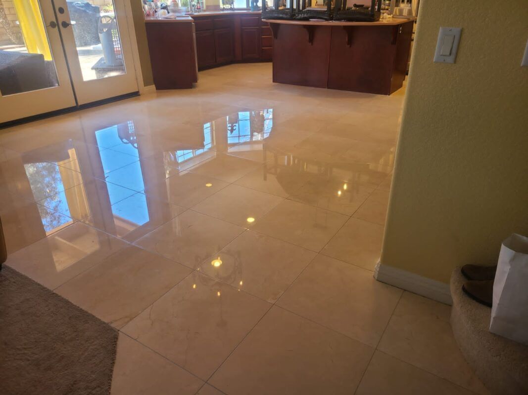 A high-gloss, light beige tile floor reflecting light and a kitchen area with dark wood cabinets.