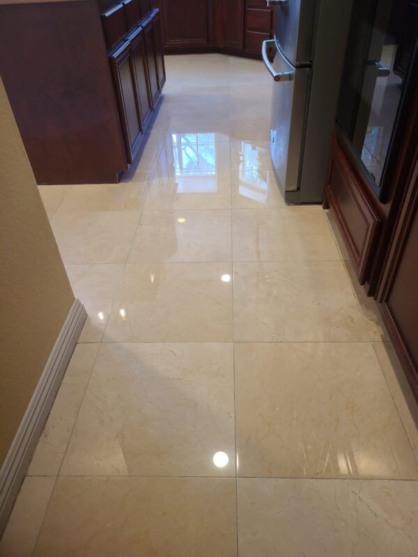 A polished, light-colored tile kitchen floor with reflections of lights and cabinetry.