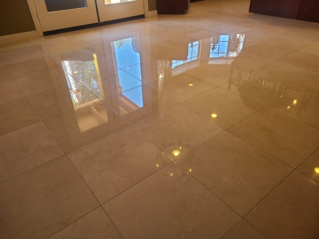 High-gloss, light-colored square floor tiles reflecting a doorway, windows, and indoor lighting.