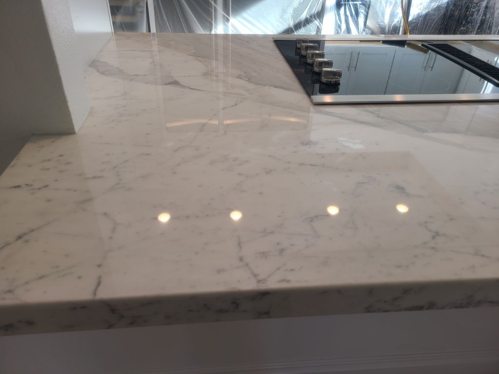 Close-up of a white marble countertop with grey veins next to a black induction cooktop in a modern kitchen.