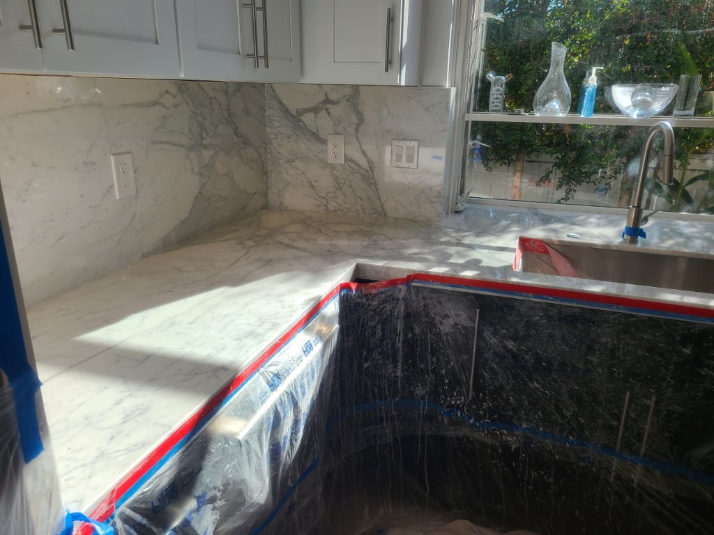 A marble countertop and backsplash installed in a kitchen, with protective plastic covering the unfinished cabinets below.