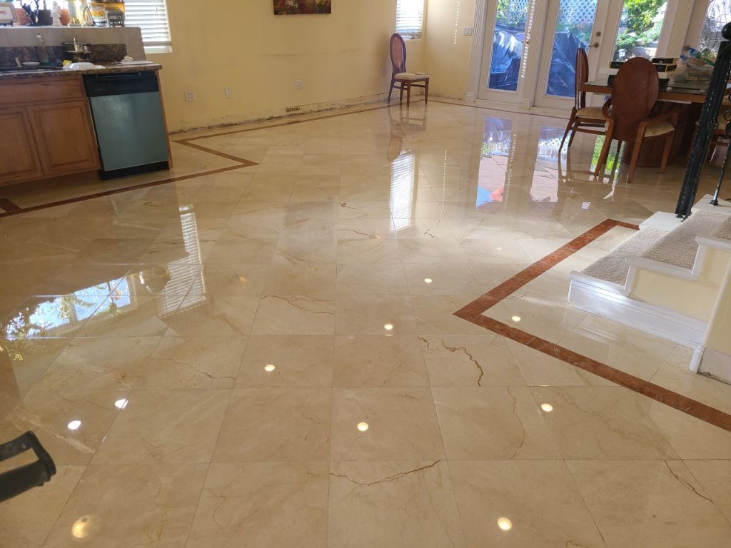 A glossy, light beige tiled floor in a bright, open-concept living area with a kitchen, dining set, and staircase.