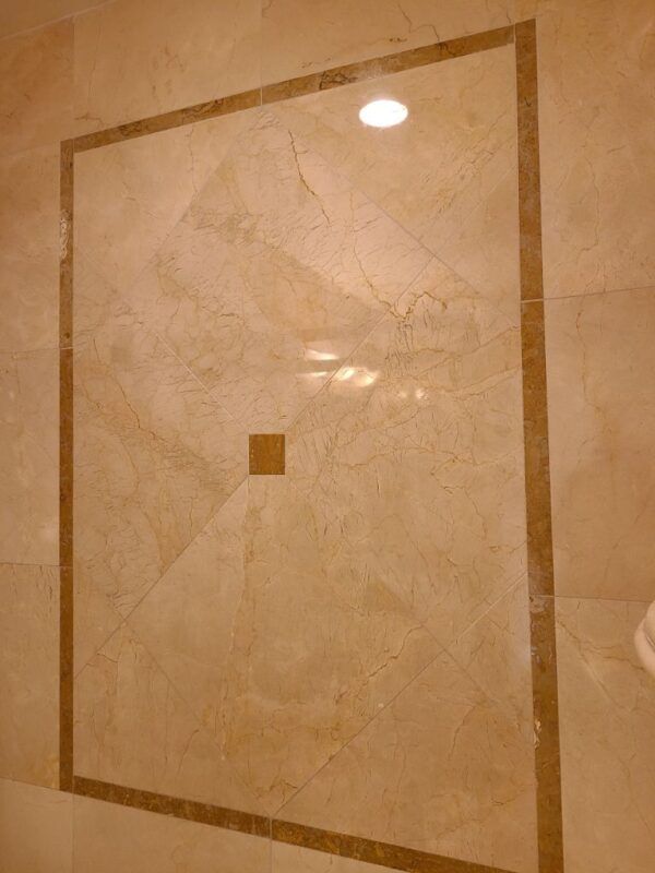Beige marble wall tiles featuring a rectangular border pattern and a small central square accent.