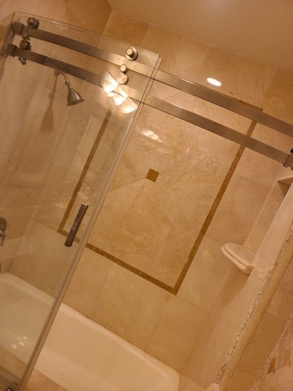 A modern tiled shower featuring a glass sliding door, a shower head, and a small built-in corner seat.