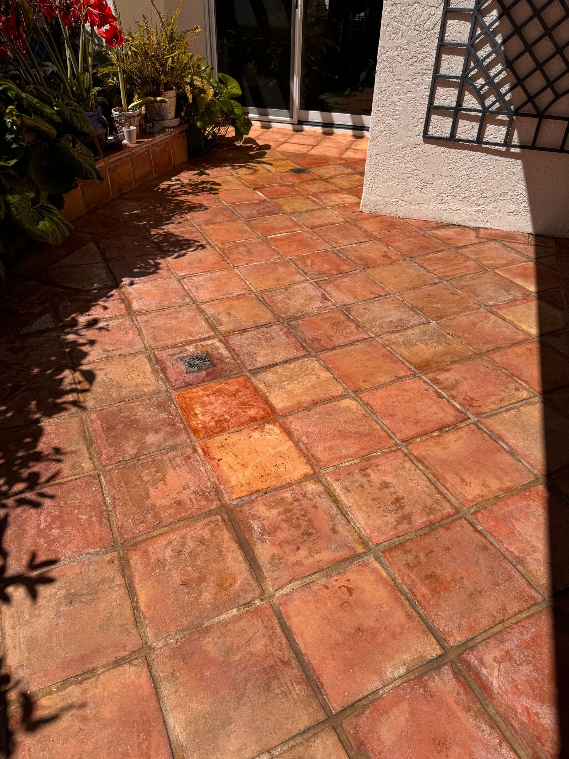 A close-up view of an outdoor patio covered in rustic, earth-toned terracotta tiles next to a white stucco wall.