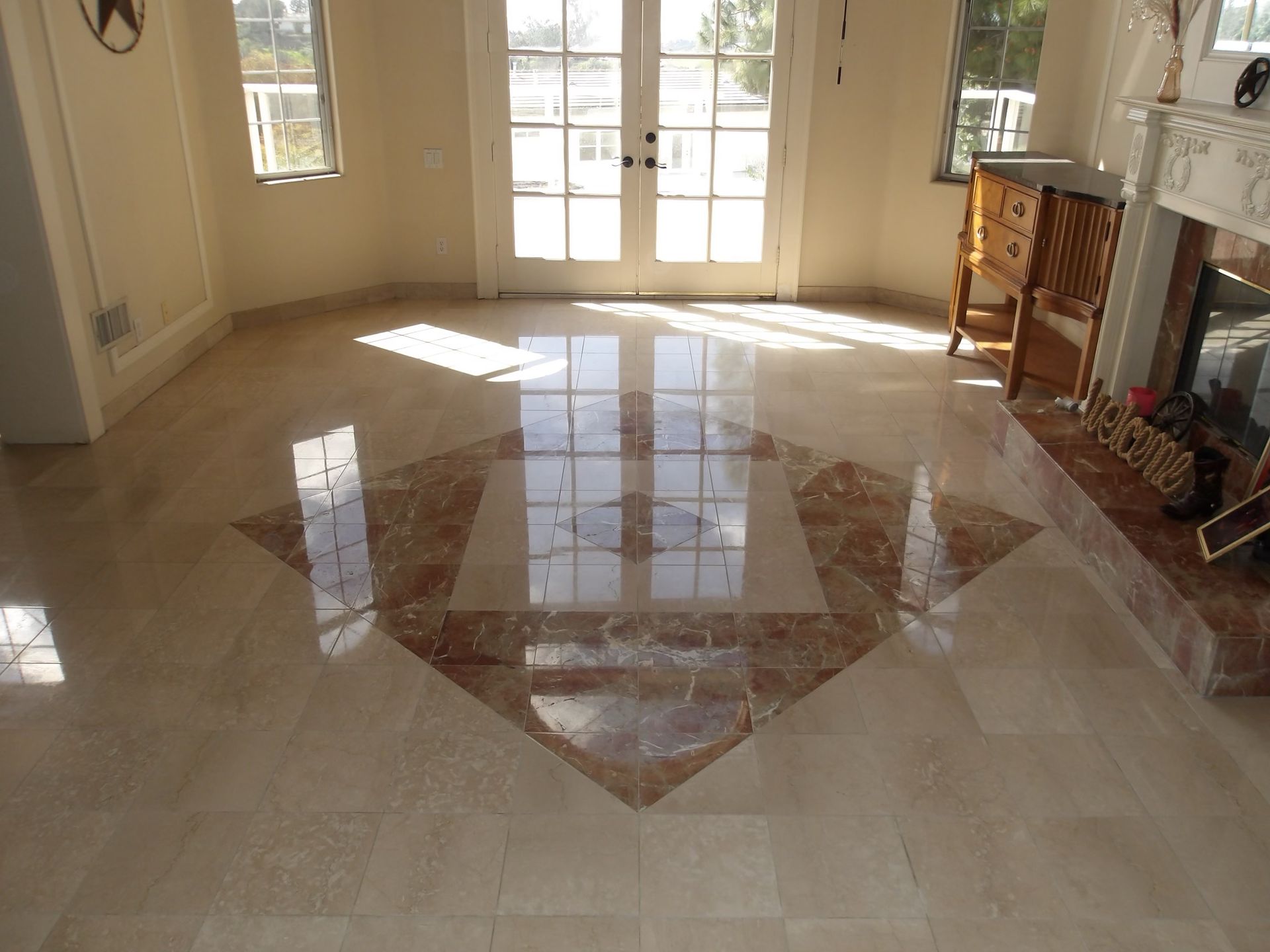 Shiny, light-colored tile floor featuring a decorative diamond-shaped inlay of brown marble in a bright, sunlit room.