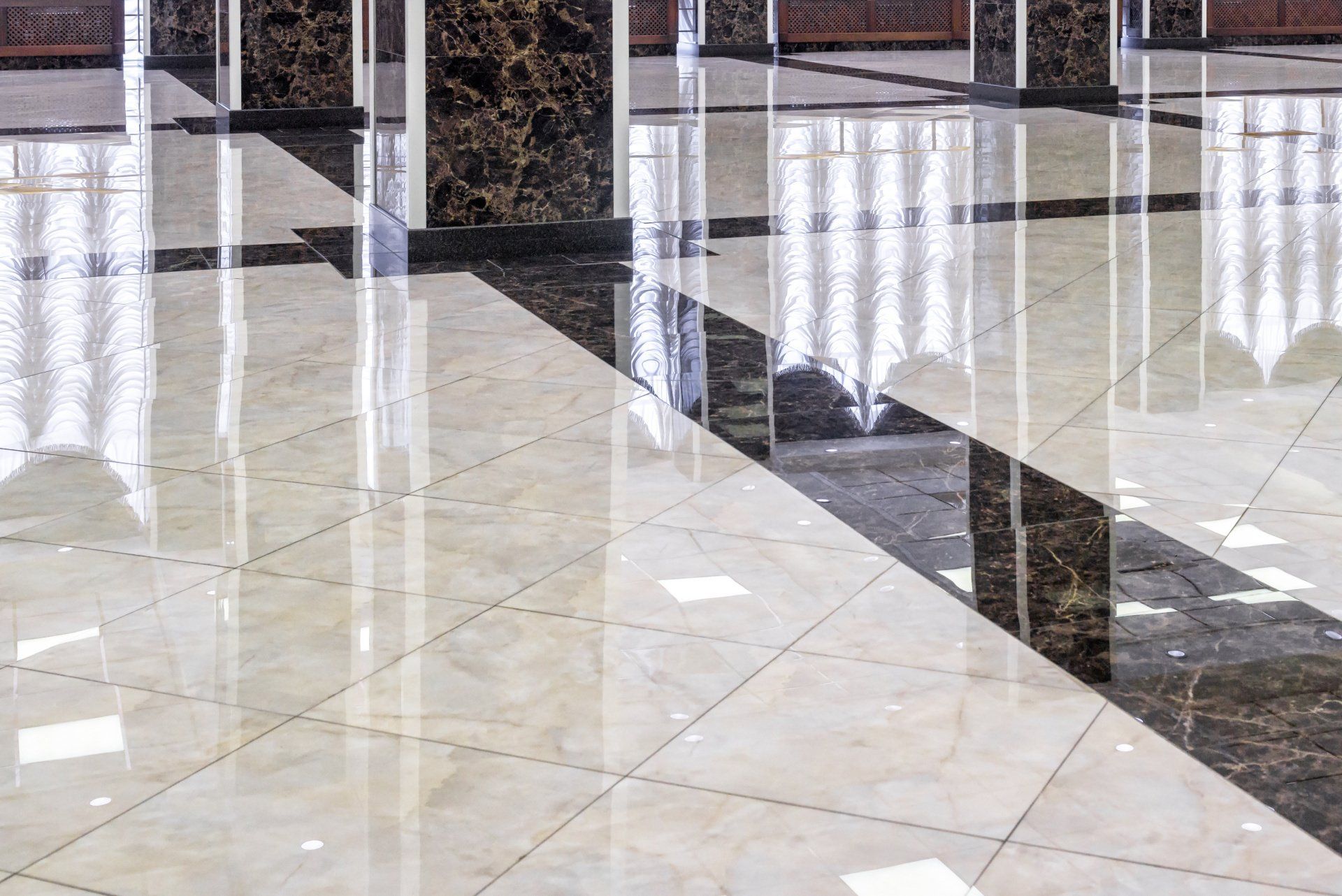 Polished floor with a grid pattern of light beige and dark brown marble tiles, reflecting light and overhead columns.