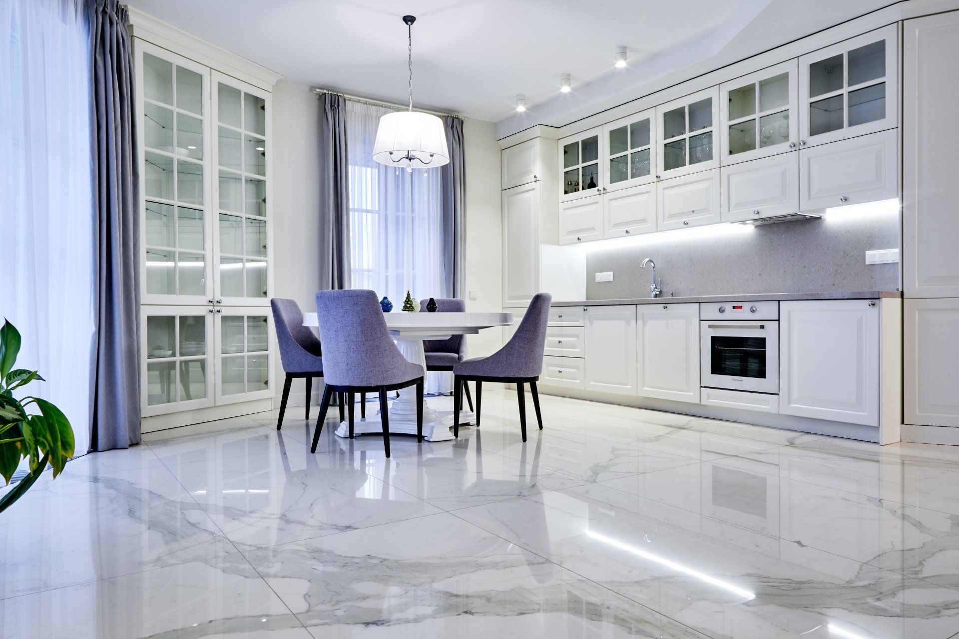 A bright, modern kitchen and dining area with white cabinets, marble floors, a round table, and purple chairs.