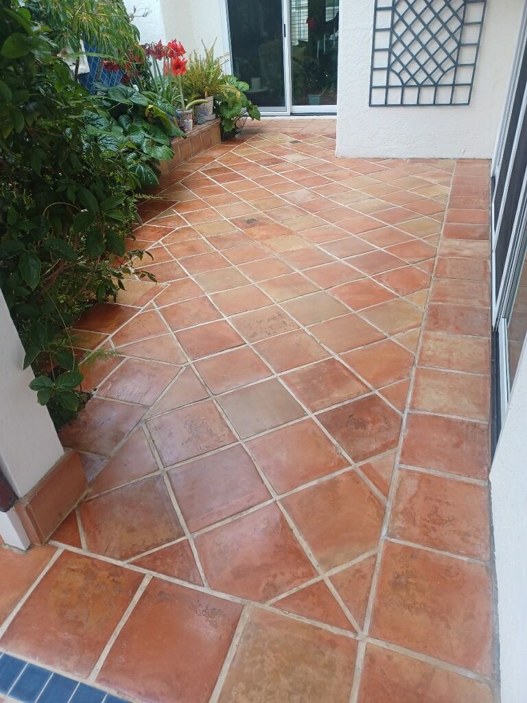 A patio featuring terracotta-colored square tiles arranged in a diagonal pattern, framed by a straight border of tiles.