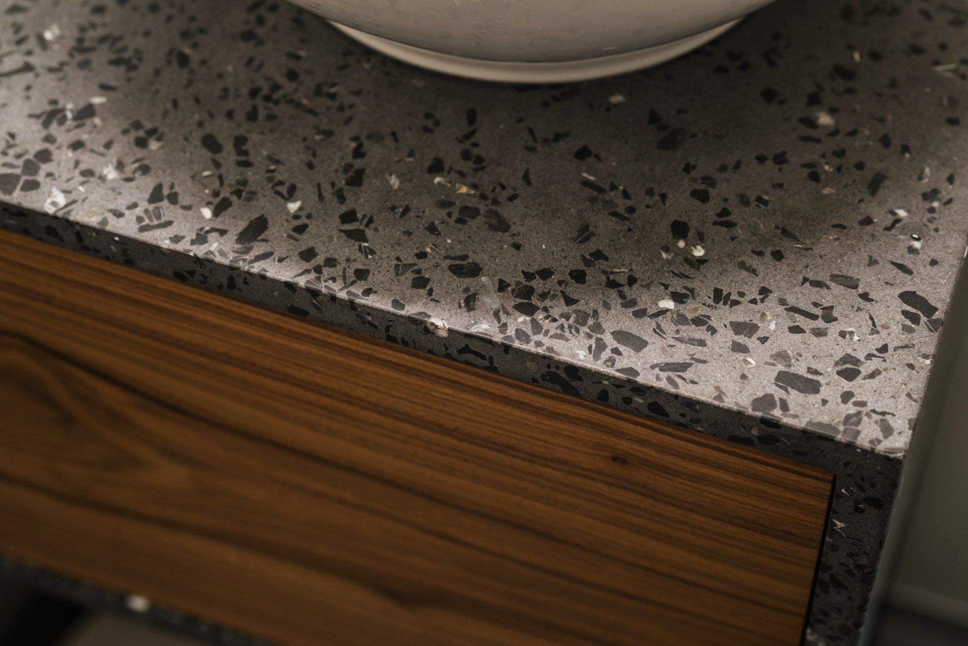 A close-up of a bathroom vanity with a dark gray terrazzo countertop and a wooden drawer front.