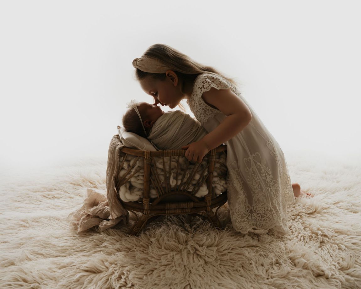 Een vrouw knielt naast een wiegje en buigt zich voorover om een ​​slapende baby op een zacht, crèmekleurig kleed te kussen.