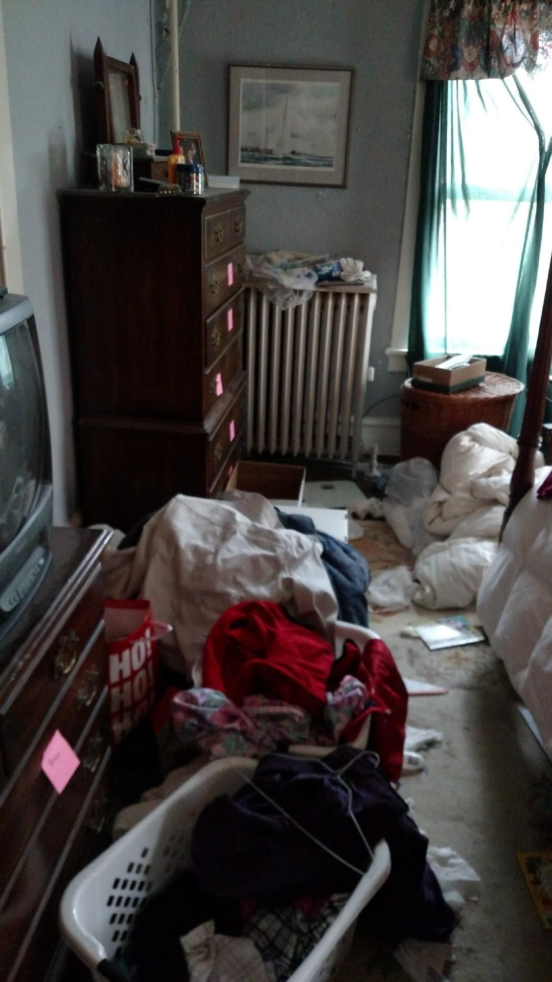 A bedroom with a lot of clothes on the floor and a television.