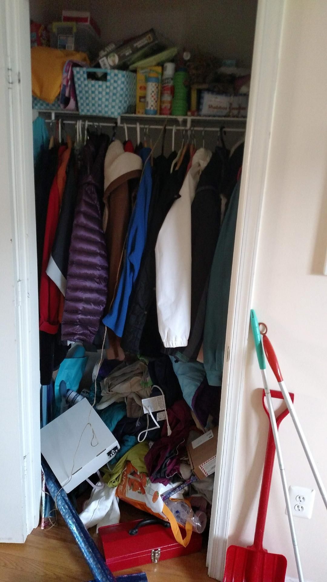 A messy closet filled with clothes and a mop.