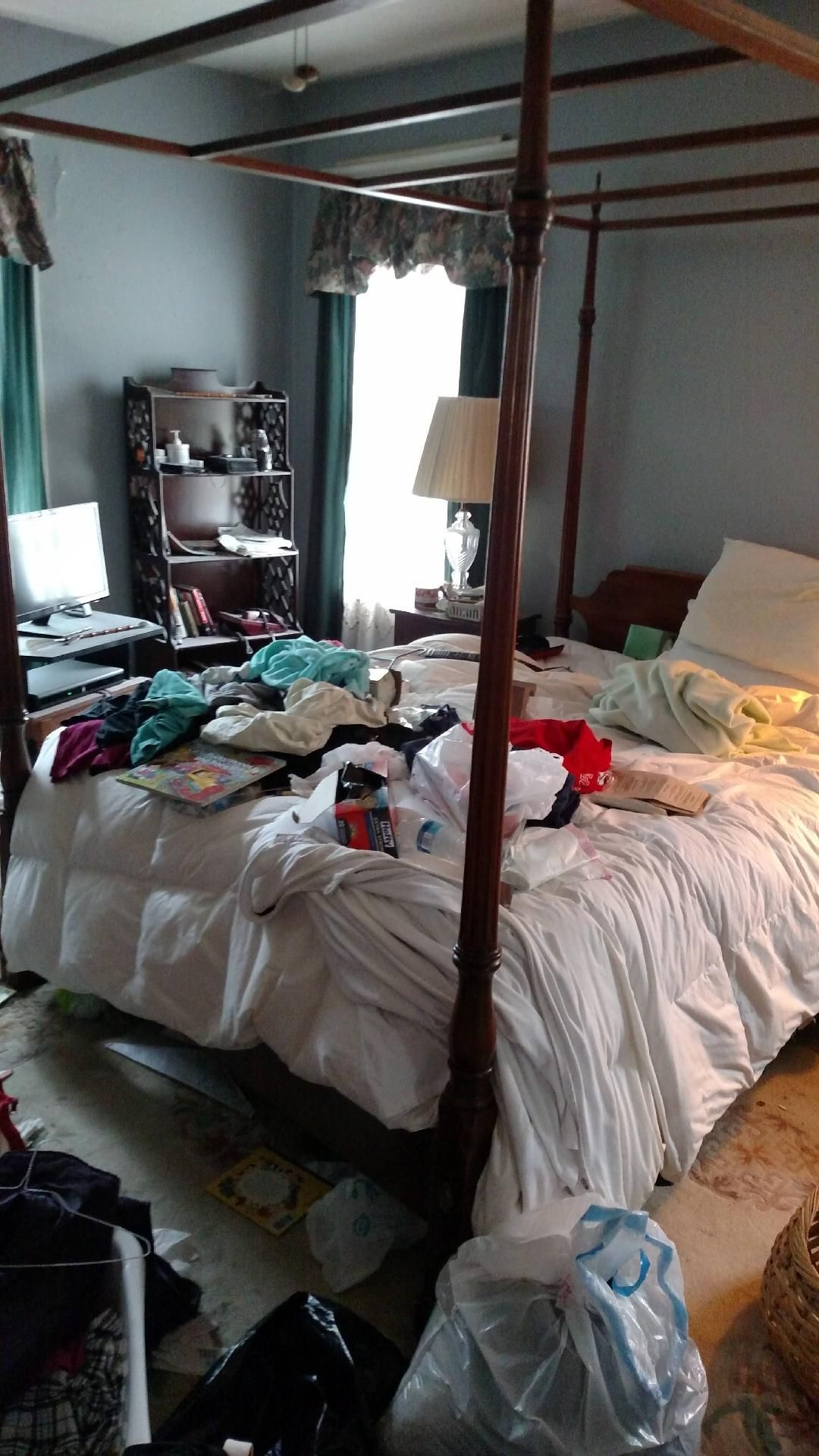 A bedroom with a four poster bed and a lot of clothes on the floor.