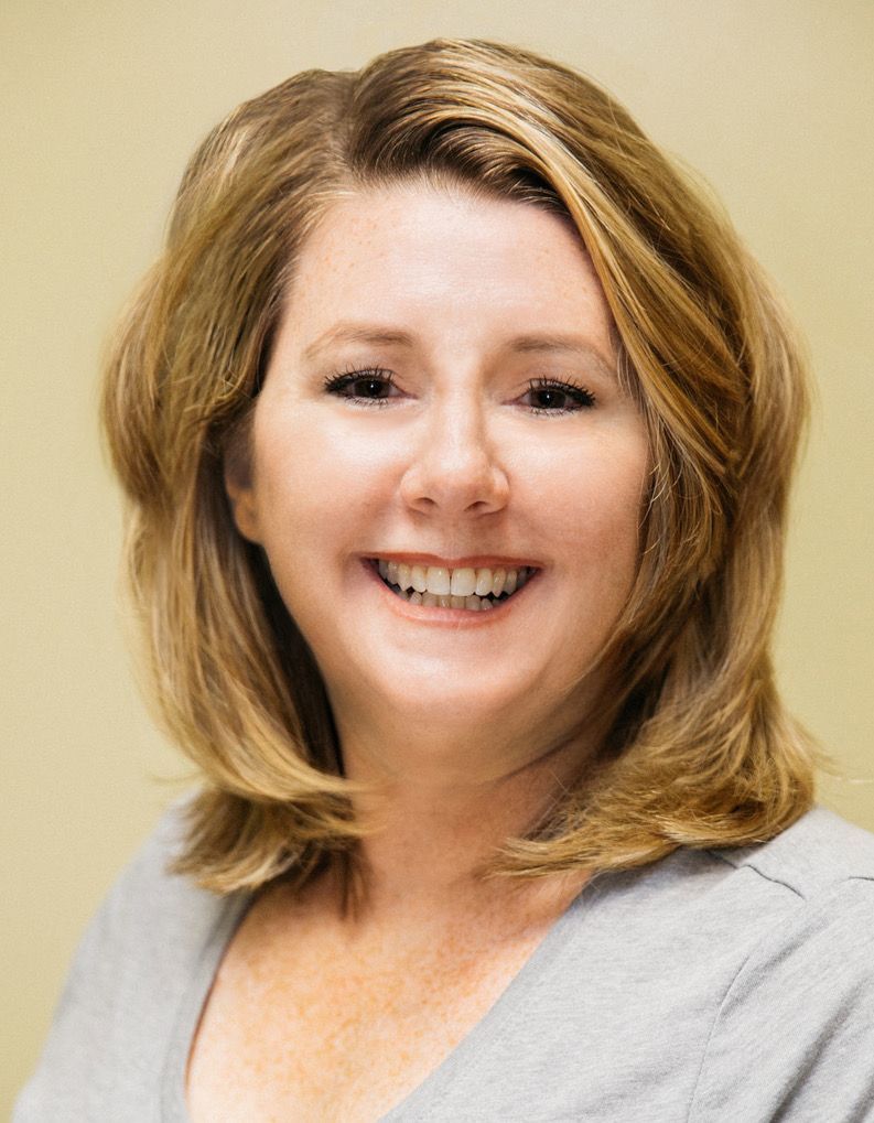 A woman is smiling for the camera and wearing a grey shirt.